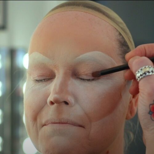 Een drag queen tijdens een make-over transformatie, met professionele make-up en styling die de artistieke expressie en transformatie laat zien