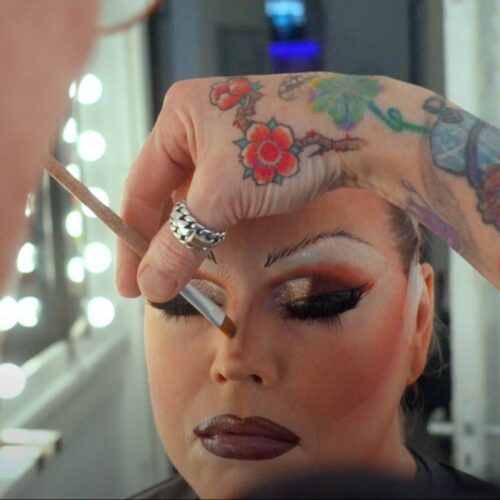 Een drag queen tijdens een make-over transformatie, met professionele make-up en styling die de artistieke expressie en transformatie laat zien